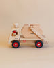 The Fagus Wooden Skip Truck, handcrafted in natural wood tones, rests on a light beige background. Made in Germany by Fagus, the truck features red wheels, a red knob on top, and movable parts for seamless loading and unloading.