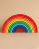 Image of the Grimm's Large Wooden Rainbow, featuring 12 colorful layers in red, orange, yellow, green, blue, and purple. This versatile and beautifully crafted toy is stained with non-toxic water-based colors and arranged in a symmetrical arch against a beige background—an ideal choice for imaginative play.