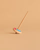 The Wooden Spinning Top - Long Stem, Red & Blue is upright on a light brown surface with a matching beige background, displaying its vibrant circular design.