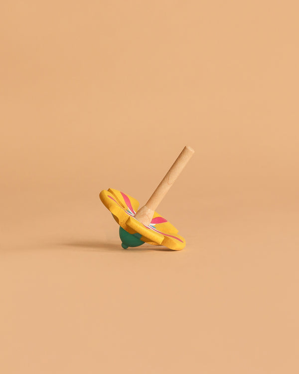 The Wooden Spinning Top - Yellow Flower, made from sustainably sourced beech wood and featuring pink and green floral designs, rests tilted on a beige surface—perfect for timeless play.