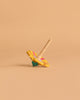 The Wooden Spinning Top - Yellow Flower, made from sustainably sourced beech wood and featuring pink and green floral designs, rests tilted on a beige surface—perfect for timeless play.
