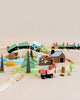 A colorful Wild Pines Train Set on a track layout with various trains, cars, trees, a logging truck toy, and other playful elements on a light beige background.