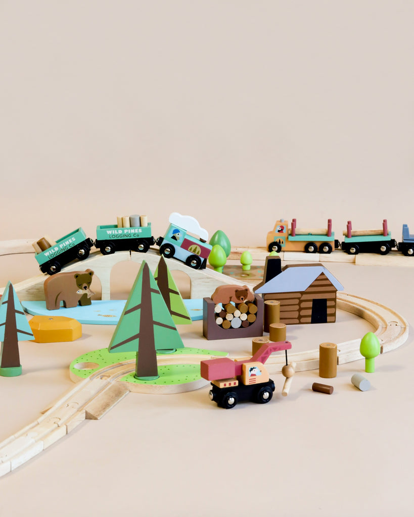 A colorful Wild Pines Train Set on a track layout with various trains, cars, trees, a logging truck toy, and other playful elements on a light beige background.