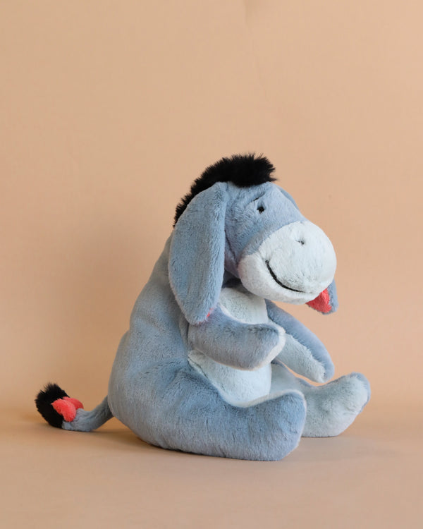 A Steiff, Disney's Winnie the Pooh Eeyore Plush Stuffed Toy, 10 Inches, sitting against a light brown background. The toy is blue with a black mane and tail tip, has a delighted