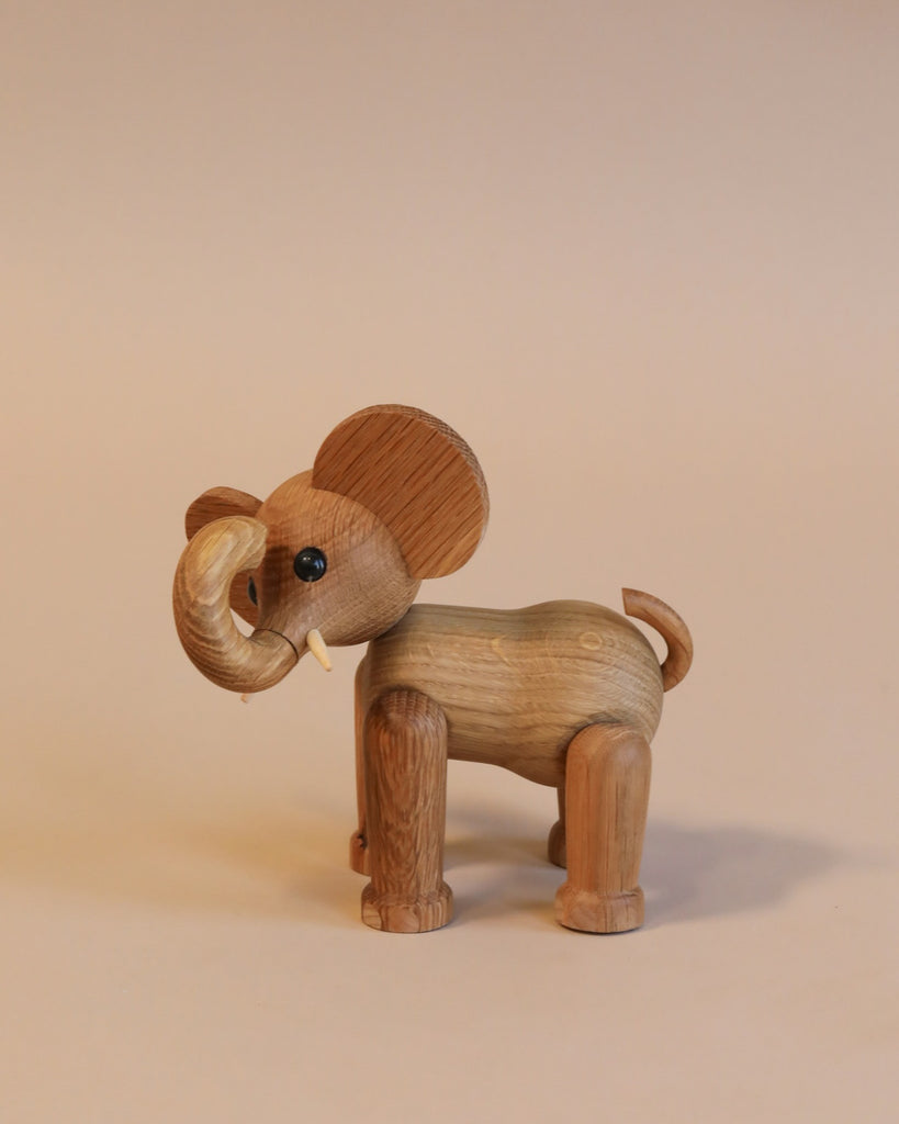 A Spring Copenhagen Ollie - Elephant toy with large ears and curved tusks stands against a plain, light beige background. Its body, crafted from FSC Oak, displays natural wood grain textures.