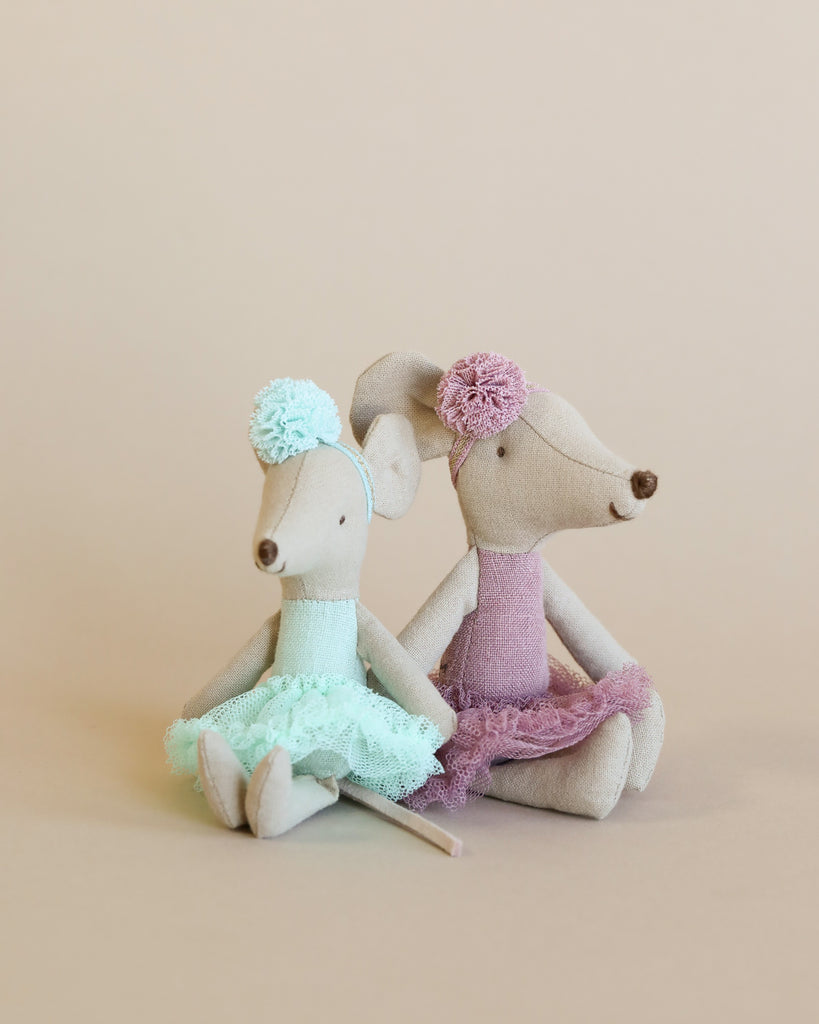 Two Maileg Ballerina Mouse - Big Sister (Heather) dolls in dresses sitting with backs leaning against each other, one in a teal tutu and the other in purple, on a beige background.