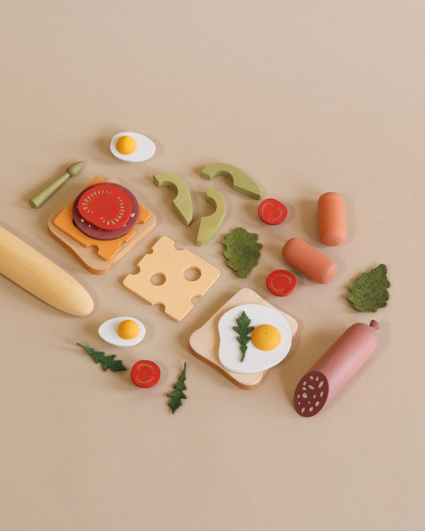 A flat lay of the Sabo Concept Handmade Wooden Breakfast Set on a beige background, all made from colorful wooden play food using non-toxic water-based paint.