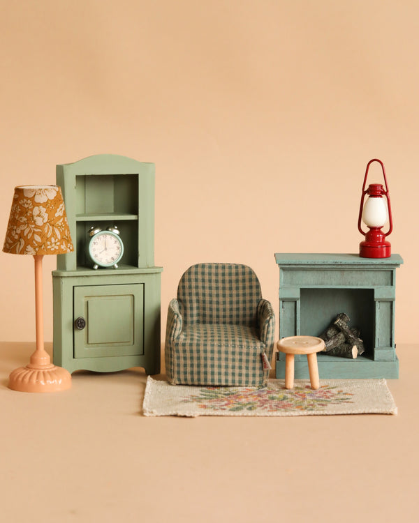 The Maileg Living Room Set features a green checkered armchair, Maileg Table & Stool, small green cabinet with clock, fireplace with lantern, floral lamp, and rug—all beautifully arranged against a beige background.