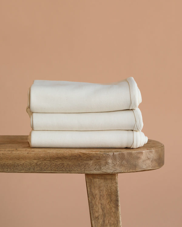 A GOTS certified Organic Baby Blanket – Natural is neatly folded and placed on a wooden bench against a plain beige background.