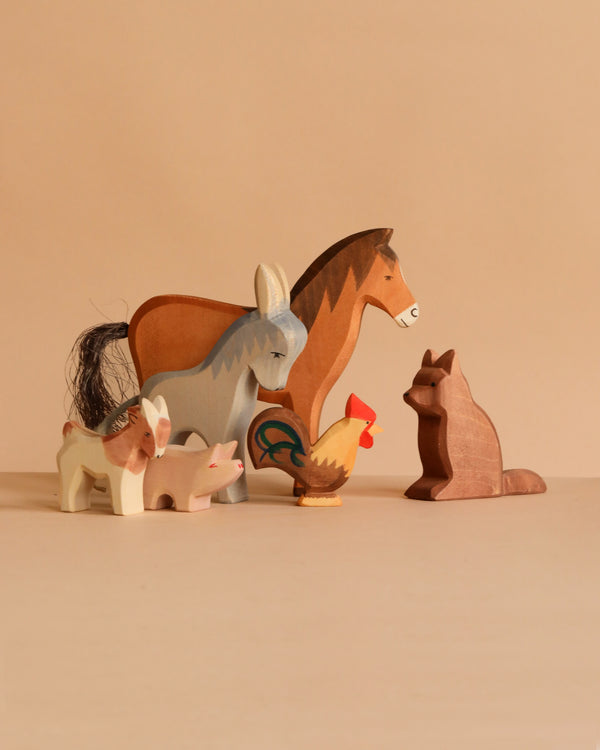 The Ostheimer Handmade Wooden Farm Animals Set, featuring a horse, donkey, fox, pig, goat, and rooster, is displayed on a beige surface with a neutral background. These handcrafted toys bring charm to any playroom.