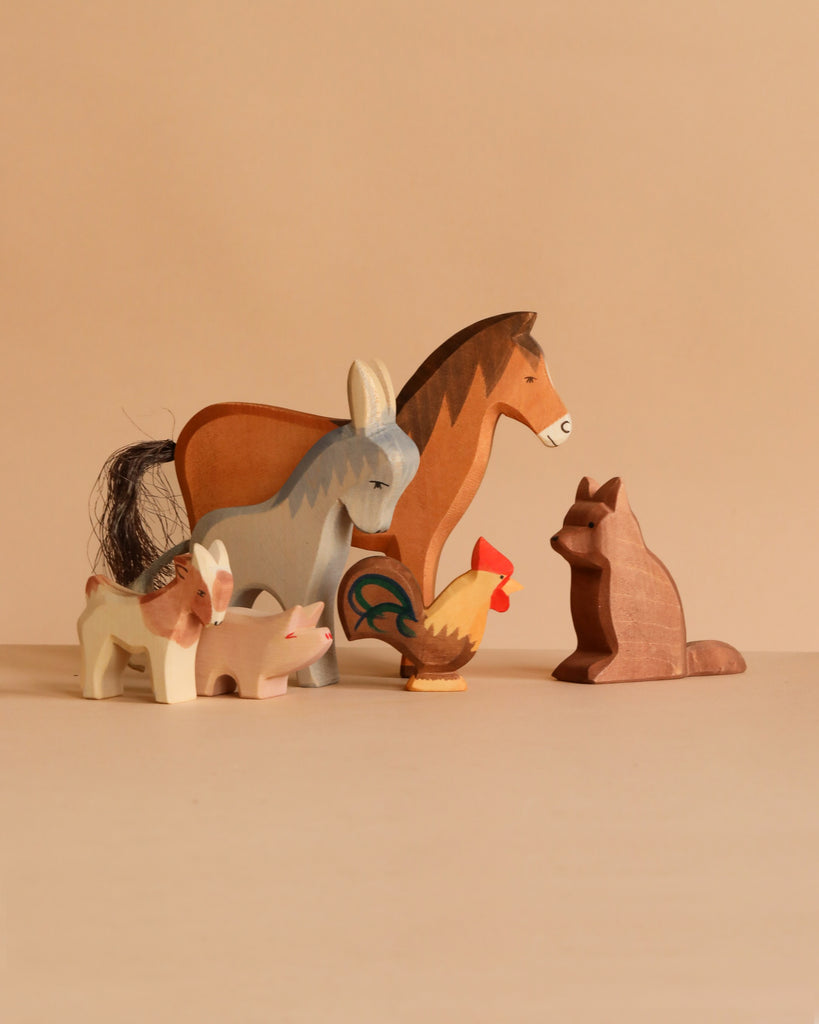The Ostheimer Handmade Wooden Farm Animals Set, featuring a horse, donkey, fox, pig, goat, and rooster, is displayed on a beige surface with a neutral background. These handcrafted toys bring charm to any playroom.