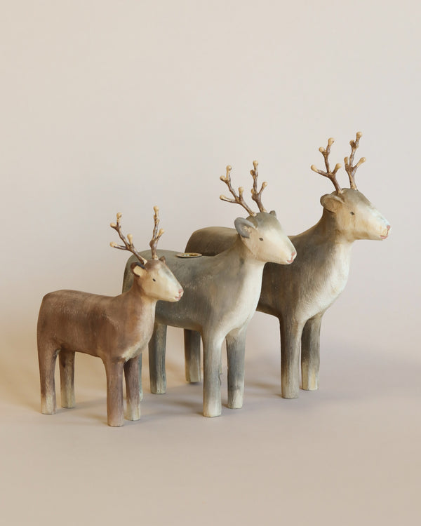 Three Maileg Wooden Reindeer Candle Holder figurines with varying shades of brown and gray, featuring detailed antlers, standing against a plain light background, sold separately.