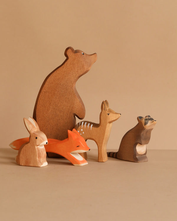 The Ostheimer Handmade Wooden Woodland Animals Set features five non-toxic, handcrafted figures—a bear, fox, raccoon, deer, and rabbit—displayed on a plain beige background for a charming nature-inspired addition to any playroom.