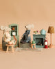 The Maileg Grandma And Grandpa Afternoon Tea set features two mice relaxing in a cozy miniature living room with pastel furniture, a tea set, pastries, books, a lamp, and a clock—perfect for charming play on a beige backdrop.