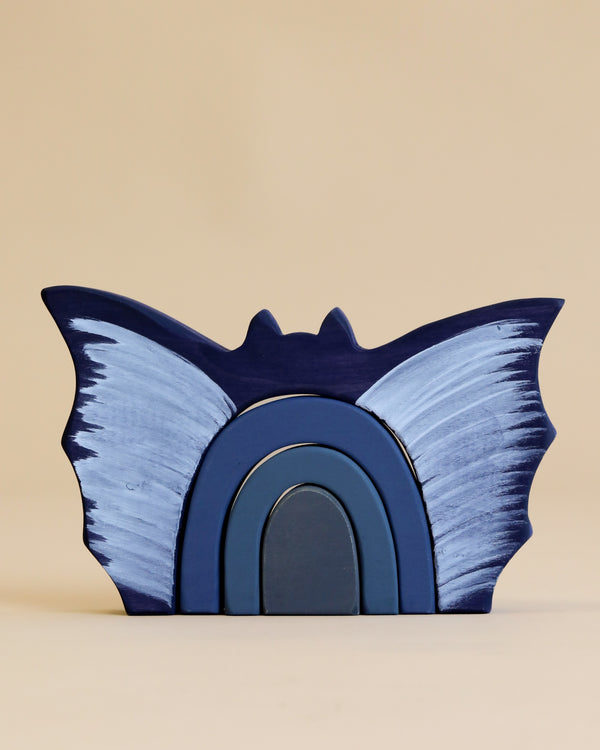 A blue artistic Handmade Wooden Bat Stacker resembling a stylized bat with spread wings, displayed against a neutral beige background.
