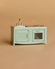 The Maileg Kitchen Set, a small mint-green piece with sink, faucet, stovetop, oven, and cabinet—ideal for dollhouse furniture—stands against a simple beige background.