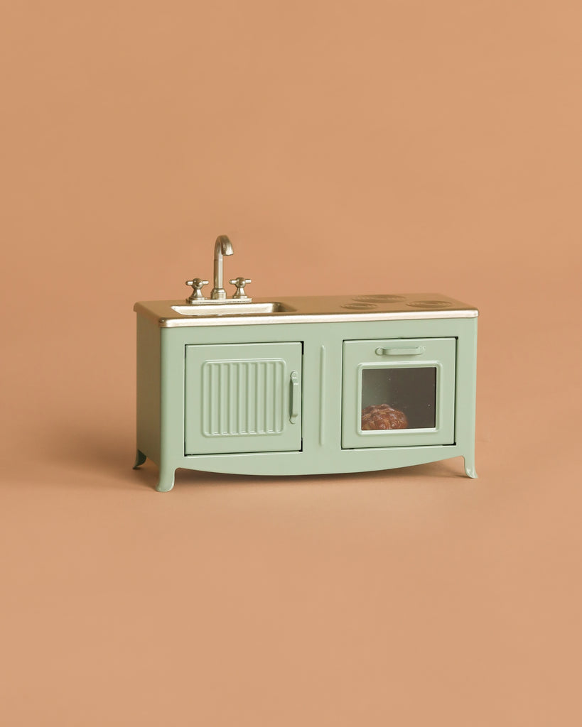 The Maileg Kitchen Set with Grandma & Grandpa, a small mint green toy kitchen featuring a sink, faucet, two doors, and a stovetop—ideal as miniature furniture for Maileg mice or adorable dollhouse accessories—is pictured on a solid beige background.