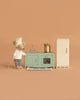 The Maileg Kitchen Set with Chef Mouse features a toy mouse chef beside a mint green stove and sink, with a pot on the stove and a beige refrigerator, all set against a plain beige background.