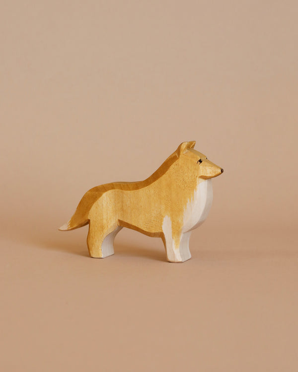 The Ostheimer Collie Dog is a small, carved wooden figure featuring a light brown body with white legs, chest, and face. With its slender build, pointed nose, small black eyes, and upright ears, this charming piece is perfect for imaginative play and fits beautifully among other Ostheimer toys on a soft beige background.