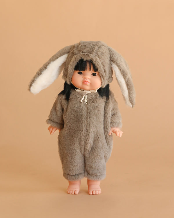 The Minikane Standing Baby Doll (14") - Jade wears a fluffy gray bunny costume with long floppy ears and stands barefoot against a plain beige background.