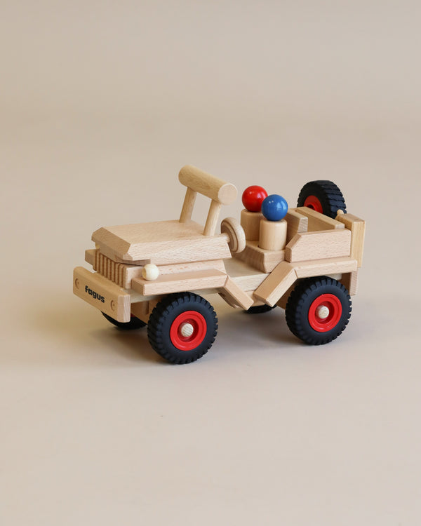 Sentence with product name: A handcrafted Fagus Wooden Jeep with red wheels and two colorful beads (red and blue) placed as passengers on a neutral background.