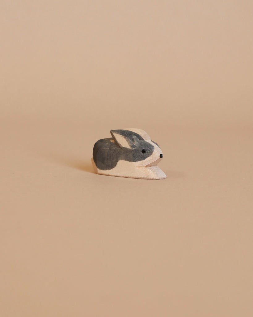 A small Ostheimer Black & White Rabbit figurine sits against a light beige background. Handcrafted with care, the wooden toy is painted in shades of gray and white, with minimalistic details giving it a simple and charming appearance—perfect for imaginative play.