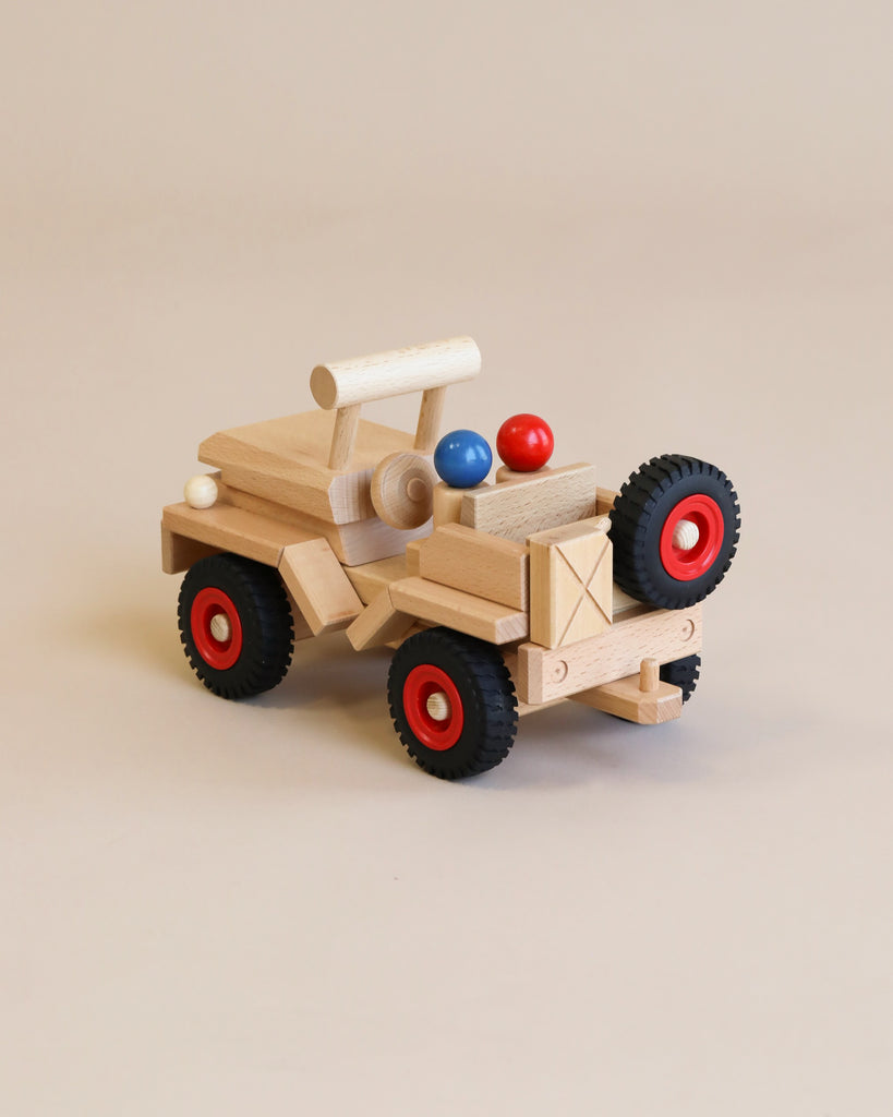 A Fagus Wooden Jeep with red and black rubber tires, featuring a cannon-like structure on top holding two colorful balls, displayed against a beige background.