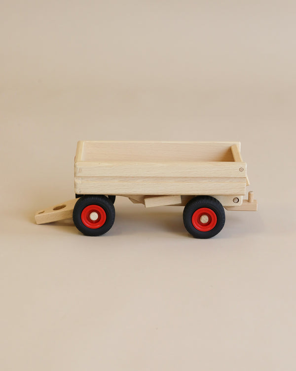 A Fagus wooden dump trailer with a simple design, featuring a flatbed and red wheels, displayed against a plain light beige background. The design is reminiscent of Fagus trucks, known for their craftsmanship and durability.