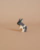 A small handmade wooden rabbit from the Enchanted Woodland Farm Set, featuring black and white patches, sits on a light beige surface with a matching background, evoking the charm of Ostheimer animal figures.