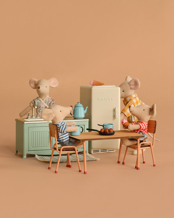The Maileg Kitchen Set with Family features four collectible mice, dressed in colorful outfits, in a miniature kitchen scene with table, chairs, stove, and fridge—perfect for simulating family meals.