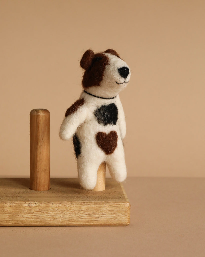 The Felt Finger Puppet: Jack Russell Terrier Dog features brown and black patches, including a heart-shaped patch on its side, and stands on a wooden platform against a beige background—ideal for imaginative play.