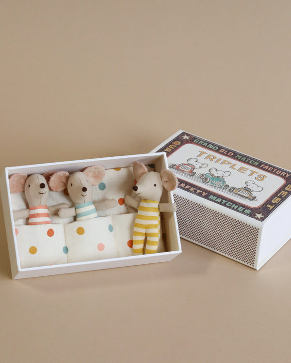 A Maileg | Triplets Baby Mice In Matchbox—likely baby mice, based on their features—dressed in cute striped and solid colored outfits, sitting inside a box labeled "grand old mice nursery rhymes.