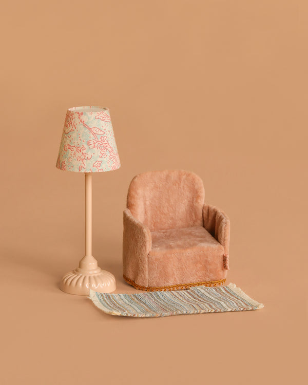 The Maileg Little Living Room Set, featuring a small plush armchair, vintage floor lamp with a patterned shade, and striped rug, is arranged against a solid beige background for a cozy, miniature living room scene.