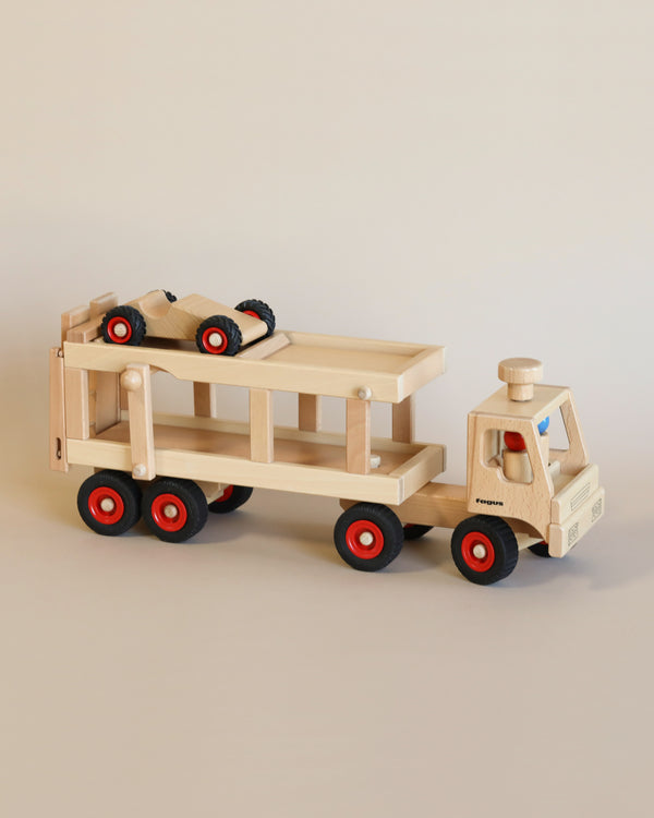 A Fagus Car Transporter with a detachable flatbed trailer carrying a small wooden car. The truck features red wheels and simple blue and black details. This Fagus Car Transporter includes peg figures for added play value.