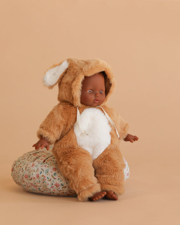 The Minikane Soft Body Doll (11") - Sidone wears a Bambi costume with a bunny-ear hood and sits on a floral cushion against a beige background.