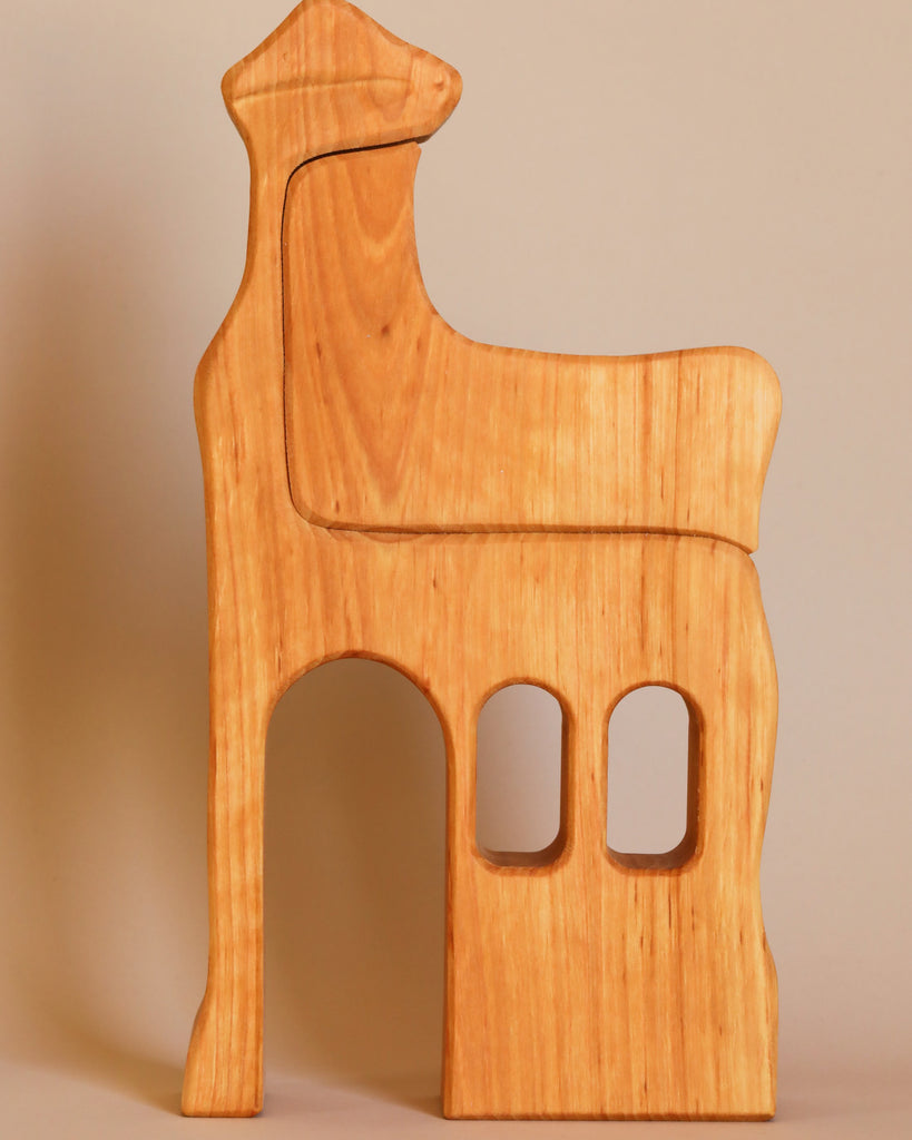 The Ostheimer Lookout - Large is a wooden camel figure, hand crafted in a minimalist style with smooth edges and natural wood grain. This camel stands upright, featuring two rectangular cutouts at the lower half that suggest legs or windows. Perfect for imaginative play, it comes against a plain beige background.