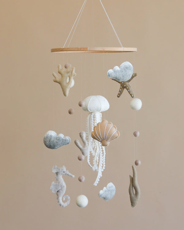 A Handmade Mobile - In The Ocean - Final Sale featuring various sea-themed elements such as starfish, shells, and clouds, all in pastel colors, suspended from a circular frame.