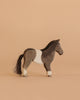 The Ostheimer Pony is a handcrafted wooden toy with dark brown, white, and light brown patches plus a black tail, displayed on a plain light brown background—ideal for imaginative play.