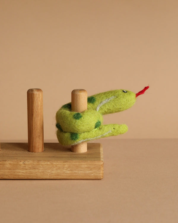 The Snake Finger Puppet, featuring green fabric with dark spots and a red tongue, wraps around a wooden peg on a small wooden base, inspiring creative storytelling and imaginative play.