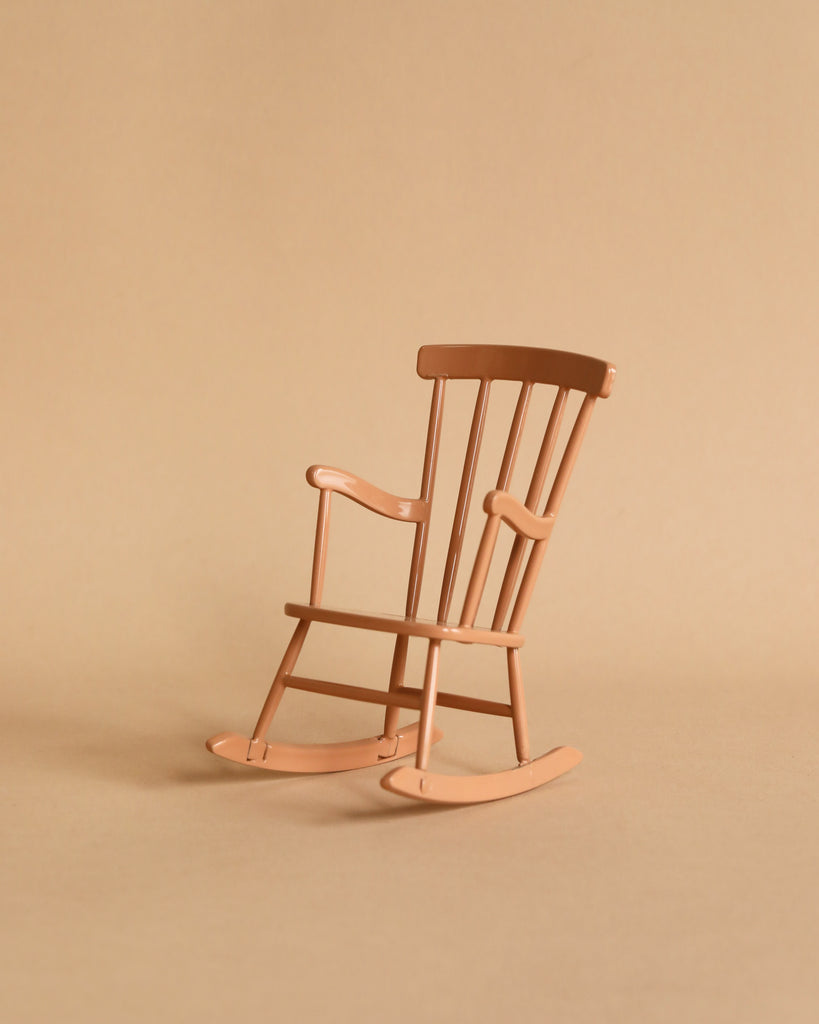 The Maileg Big Sister Bedroom Set features a small wooden rocking chair with curved runners, vertical backrest slats, and smooth armrests—ideal for dollhouse furniture. It sits on a beige surface matching the background.