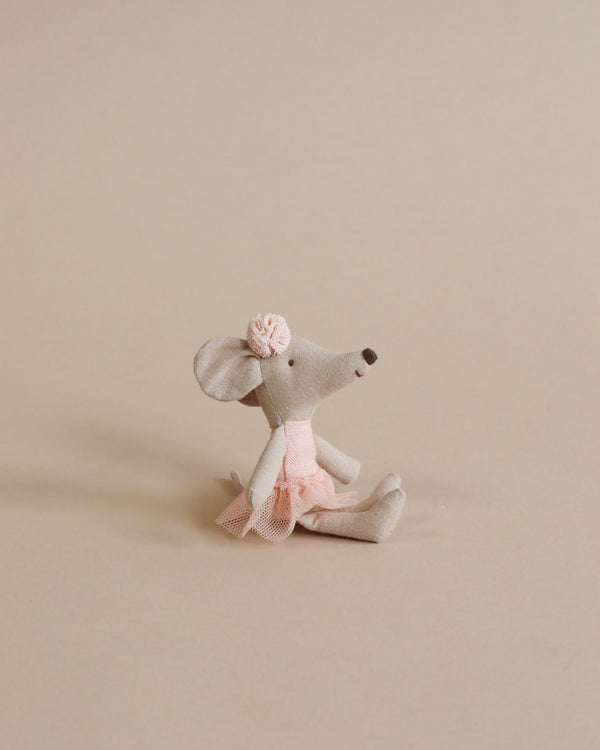 A Maileg Ballerina Mouse - Little Sister (Light Pink) in a rose tutu and bow sits on a plain beige background, appearing to gaze upward. The mouse is delicately crafted with noticeable stitches and soft features.