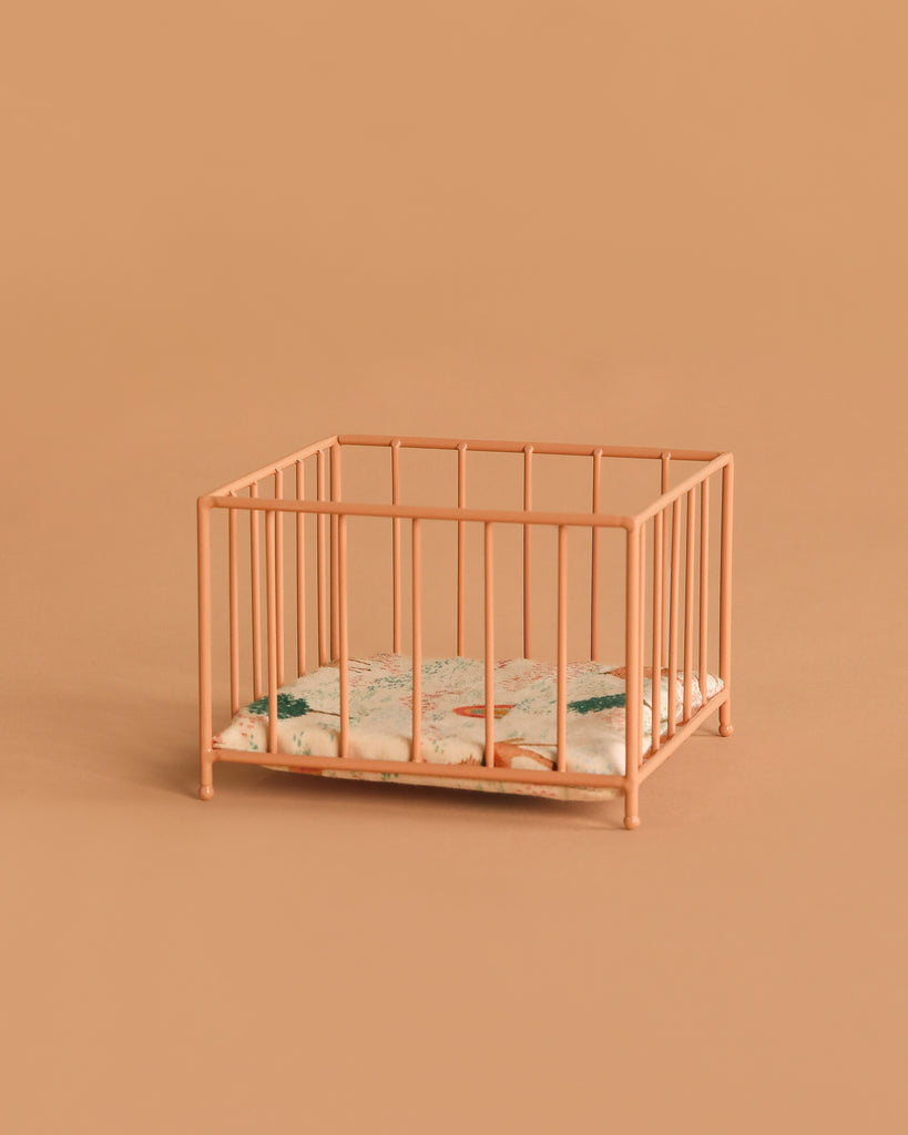 A small Maileg Playpen, Micro - Dark powder stands on a matching background. Inside, a thin mattress with a green and brown floral pattern adds charm to this micro-sized playpen.