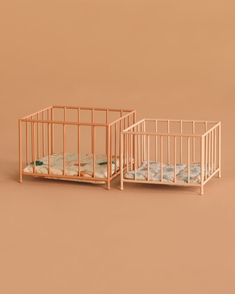 Two Maileg Playpen, My - Rose with patterned mattresses are placed side by side on a beige background. The playpens have a similar design but vary in size.
