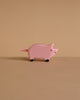 A small, pink pig figurine from the Holztiger Handmade Wooden Animal Play Set with black feet stands on a beige surface against a matching background, showcasing the charm of European craftsmanship.