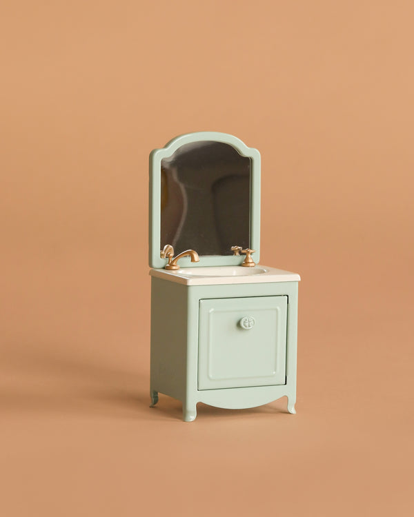 The Maileg Sink Dresser With Mirror, Mouse - Mint is a pastel green play sink with a gold faucet, cabinet, and mirror—ideal for completing your Maileg mouse house or toilet bathroom scene.