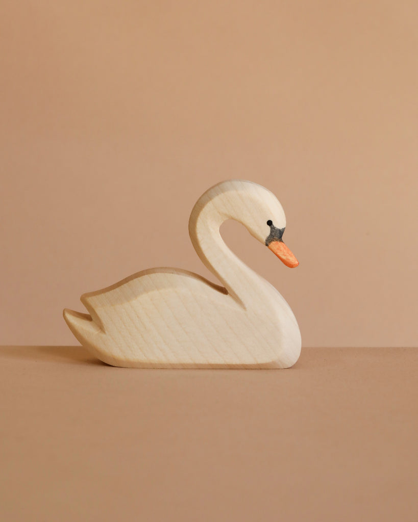 The Ostheimer Handmade Wooden Swan Family Set, featuring white bodies with orange beaks and black detailing, is displayed on a neutral brown surface against a matching solid brown background.