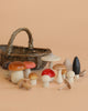The Forest Mushrooms Basket - Moon Picnic features an assortment of wooden mushrooms in various shapes, sizes, and colors, arranged for imaginative play in front of a rattan basket on a beige background.