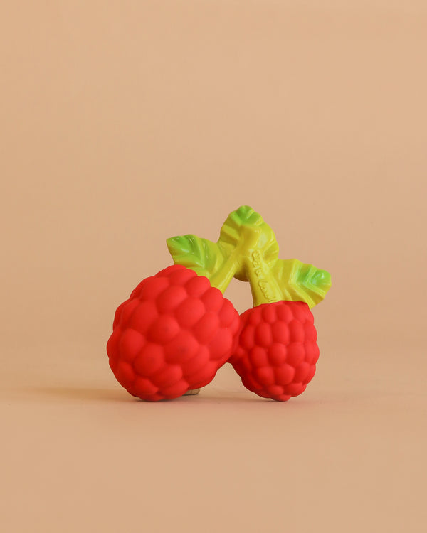 Valery the Raspberry Teething Toy is a brightly colored sensory teether made of natural rubber, shaped like two raspberries with green leaves, displayed on a plain, peach-colored background.