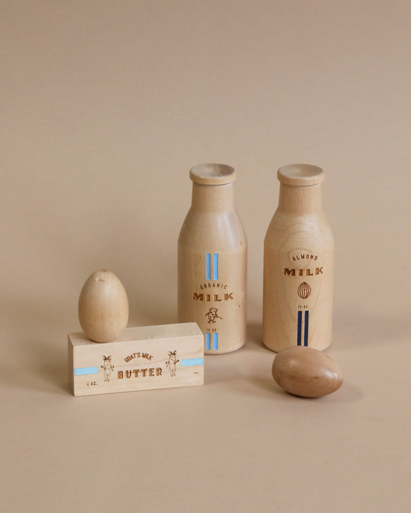2 natural color wooden milk bottles, one wooden natural color egg in front of the milk bottle.  One wooden stick of butter with one wooden natural color egg on top of stick  of butter. 