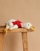 The Steiff Gilda Christmas Goose with Red Scarf rests softly on a wooden bench against a beige background—an ideal cuddle companion or delightful holiday gift.